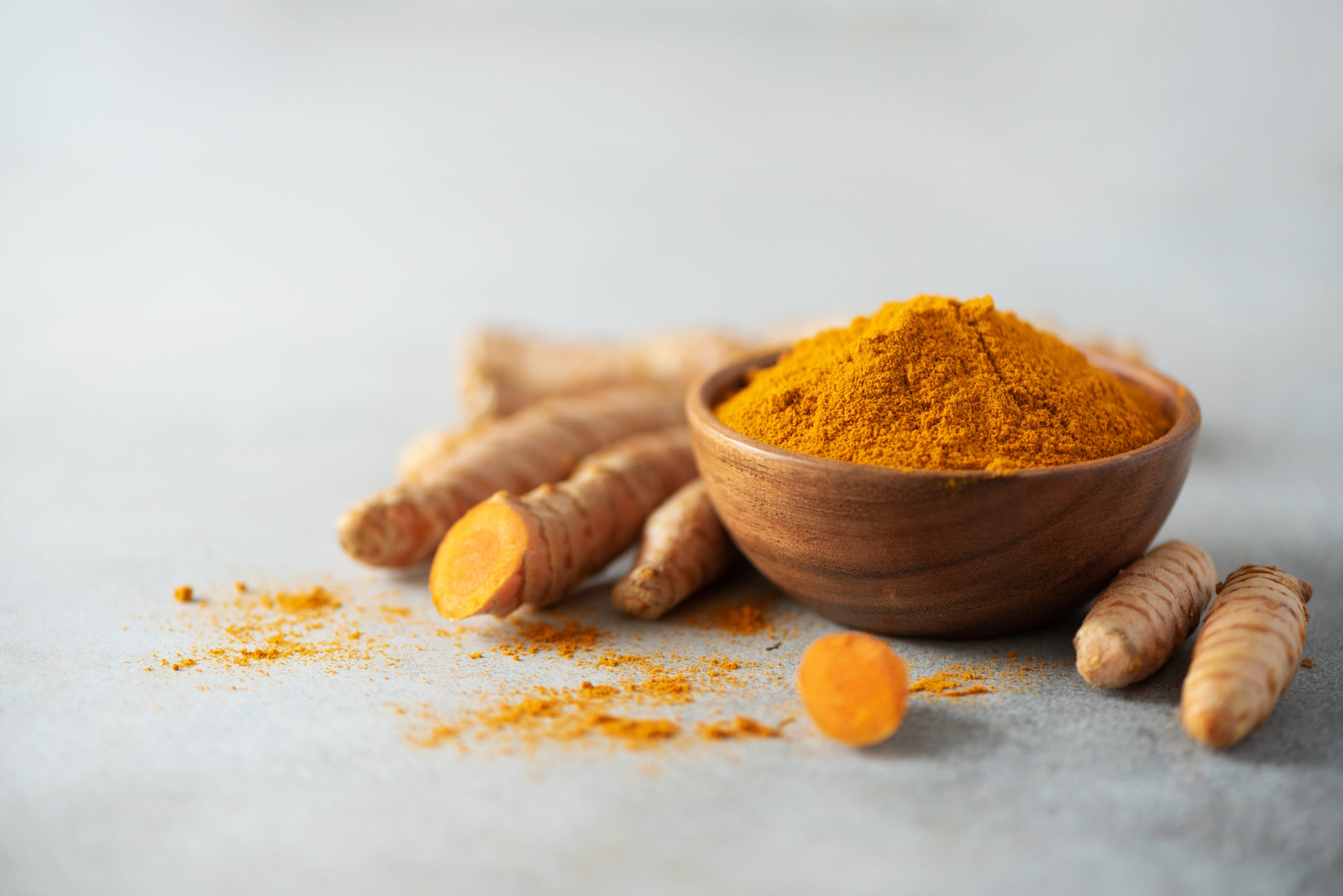 Turmeric powder in wooden bowl and fresh turmeric root on grey concrete background. Banner with copy space